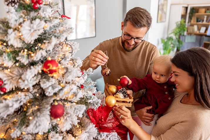 Family decorates for Christmas. Family hangs baby's first personalized Christmas ornament on the tree. 